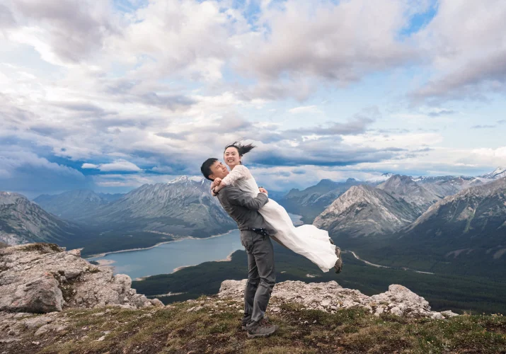 The groom lift the bride at the end of their hiking adventure with Banff Wedding Photographers. They are both happy.