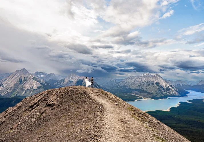 Newlyweds walk on the ridge of the mountain with the panoramic view on the Canadian Rockies a the lake.
