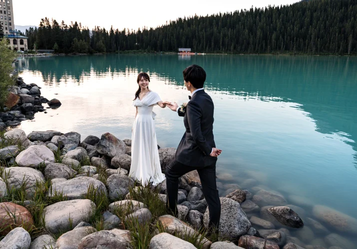 Groom helps his wife while walking on the rocks at the Lake Louise.