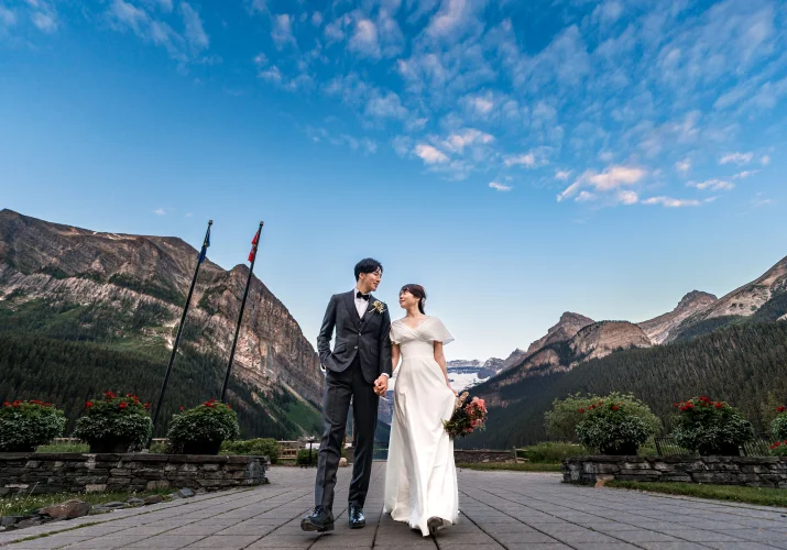bride and groom walk on the pavement at the Lake Louise hotel. Above them blue sky.