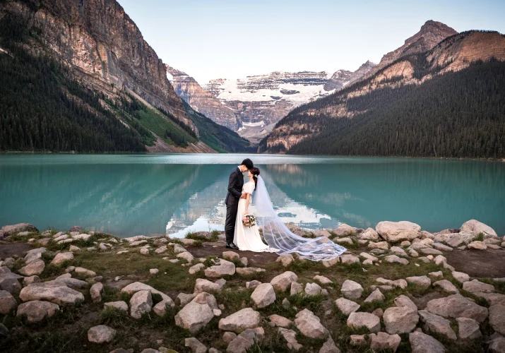 Newlyweds in a hug surrounded by the Canadian Rockies and turquoise Lake Louise.
