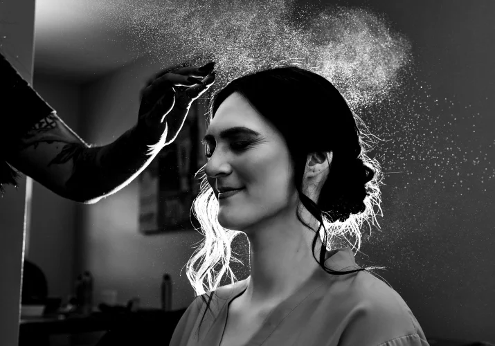 Creative photograph of the maid of honor getting her hair done with the back light on heir har and a drops of the spray.