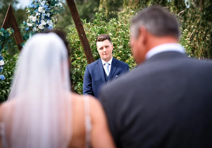 father of the bride walking her down the aisle while the groom look at her with love and excitment.