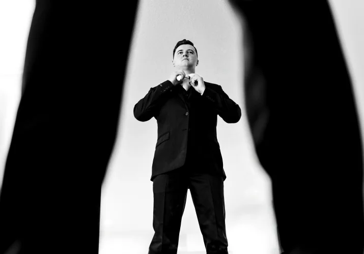 the groom fixes his tie. Photograph taken by Calgary wedding photographer through his legs