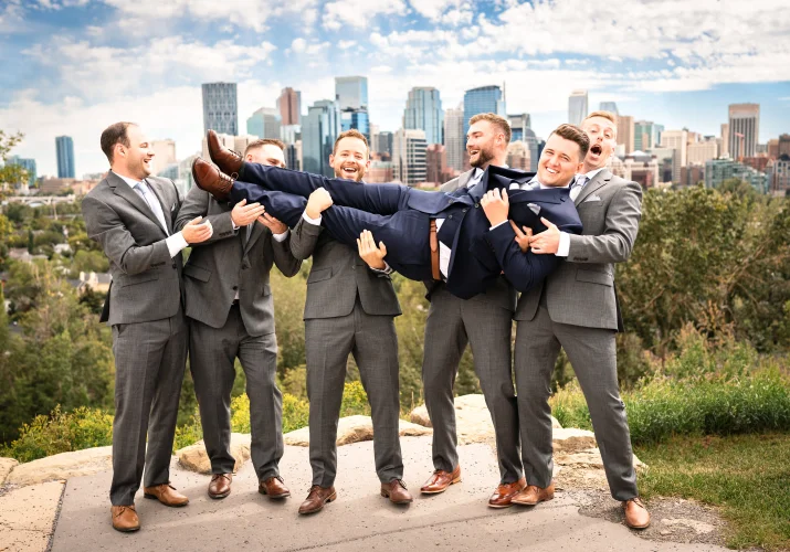groomsmen take the groom on their hands. Photo taken against the city of Calgary.