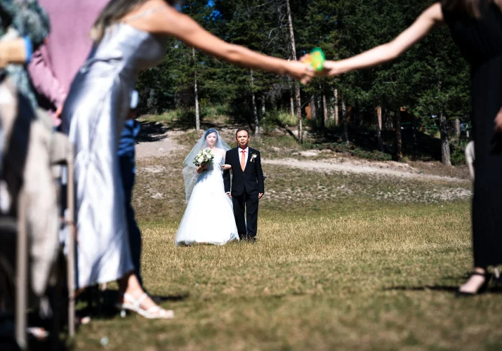 Father on the bride walks her on the aisle at Turner Mountain in Banff. Quest is passing the bubbles on hand to hand while they are walking.