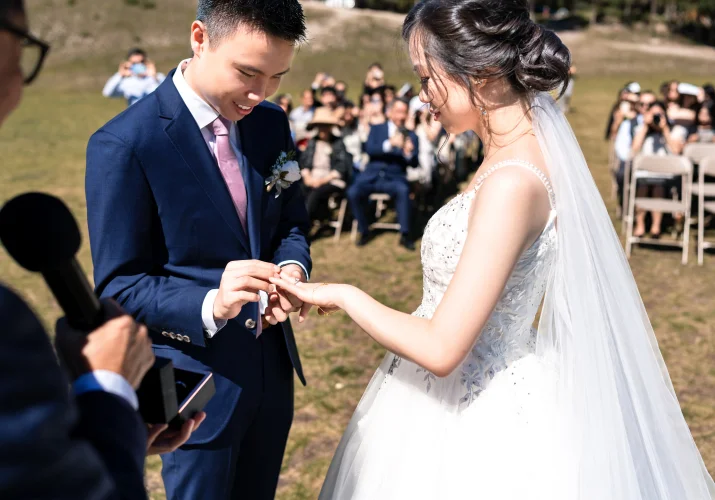 the groom puts the wedding ring on the bride's finger while all the banff wedding quests watching