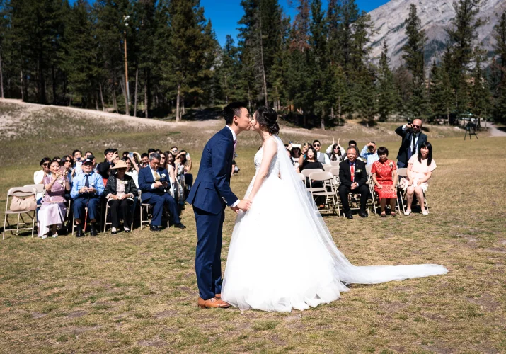 first kiss on the newlyweds in Banff. Guests on the chairs watching them.