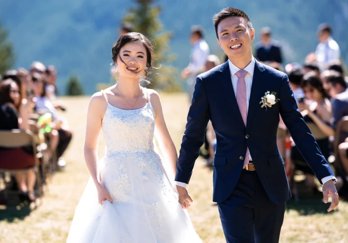 newlyweds walk out the aisle at the Banff Wedding Ceremony. They both smile and hold hands.