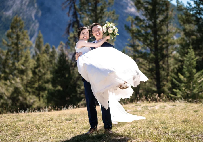 the groom carry his wife on the hands. They both smile. Moment captured by banff wedding photographer.