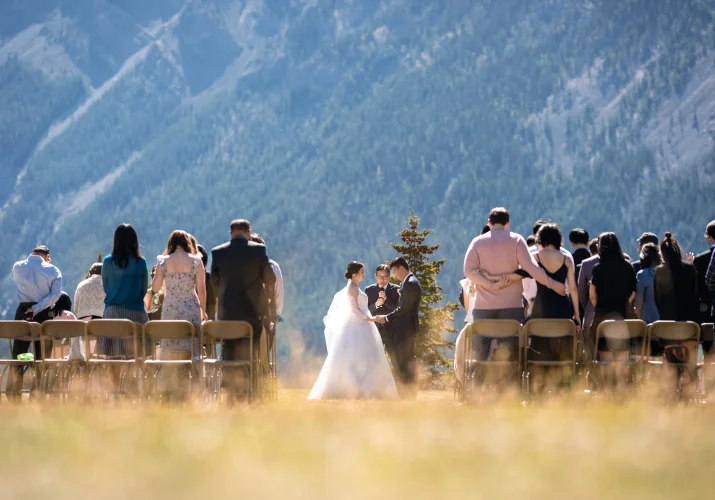 Banff Wedding Photography at Tunnel Mountain. Photograph at the wedding ceremony of the banff officiant , newlyweds and the quests standing and watching then.