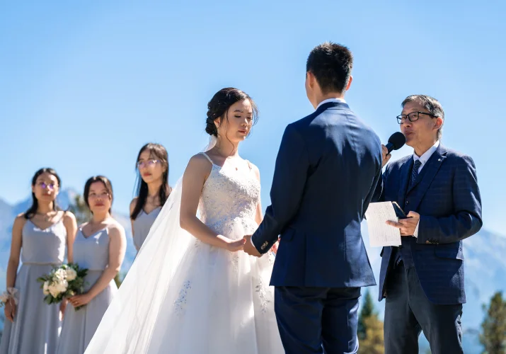 bride and groom hold their hands while banff officient giver them blessing.