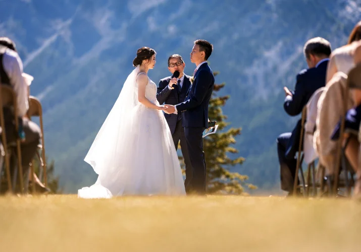newlyweds holding hands and the officiant holding the micophone on the Tunnel Mountain in Banff.