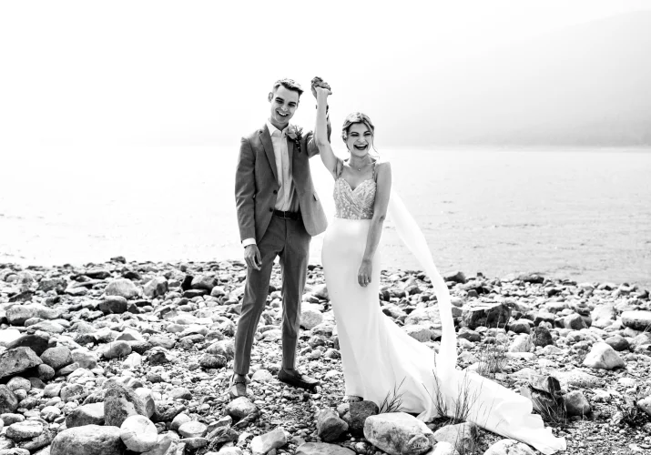 A picturesque scene of a bride and groom standing on rocks by the water, radiating love and happiness.