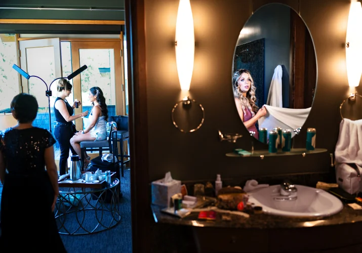 Bride getting her make up done and the bride's maid look at the mirror on the wedding day in Calgary