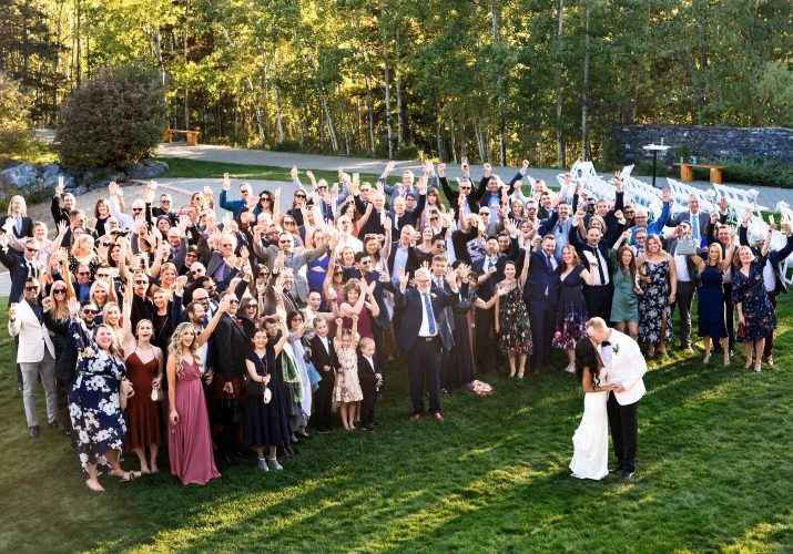 Wedding group photo with all the wedding guests while bride and groom share a kiss