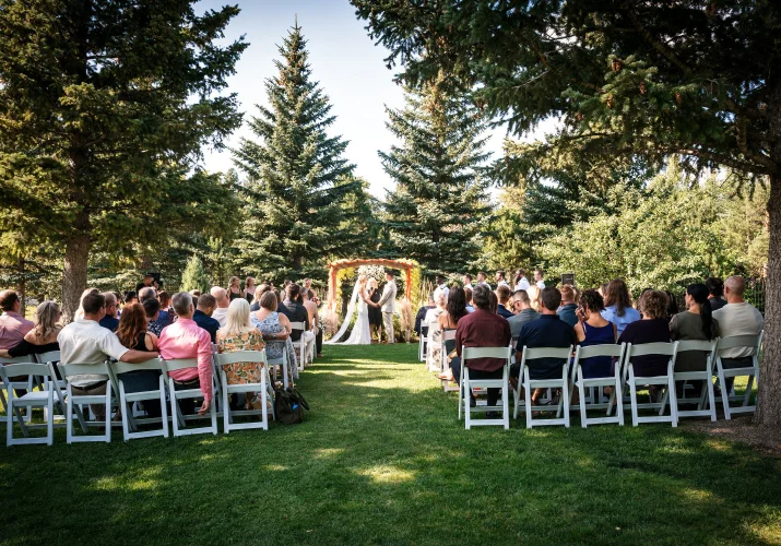 Wedding ceremony in Waterton. Quests sit on the white chairs while bride and groom echance their vowes.
