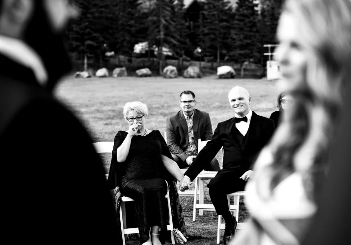 Parents of the bride hold their hands and look at their kids getting married in Banff