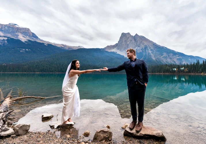 Groom helps the bride to walk on the rocks by Emerald Lake.
