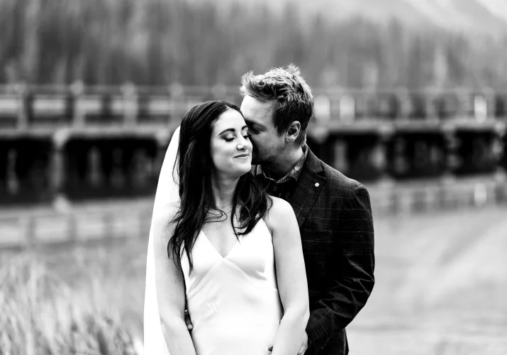 Groom hugs the bride from behind and kisses her.