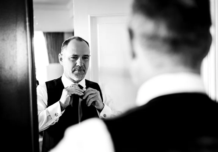Groom fixes his tie in front of the mirror.