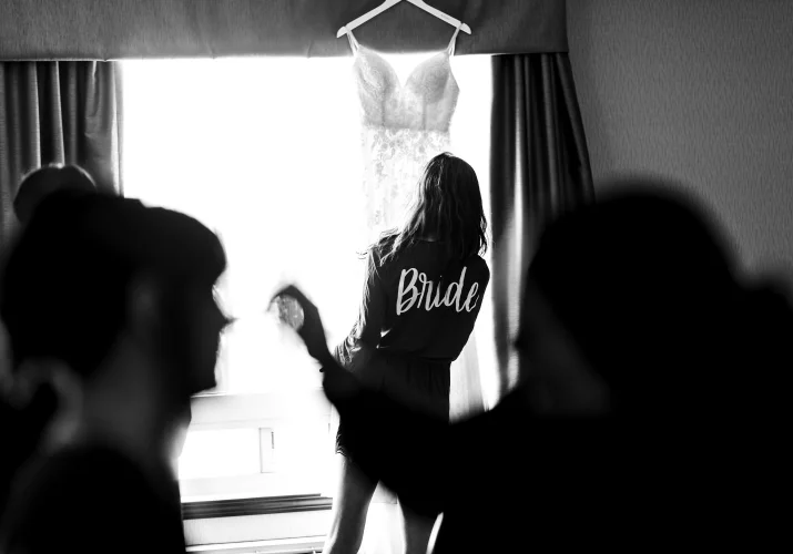 The bride looks at the wedding dress hanging on the windoe in Cagary