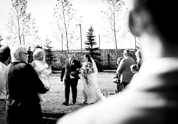 Father walks the bride down the aisle in Calgary while the groom and quests looking at them .