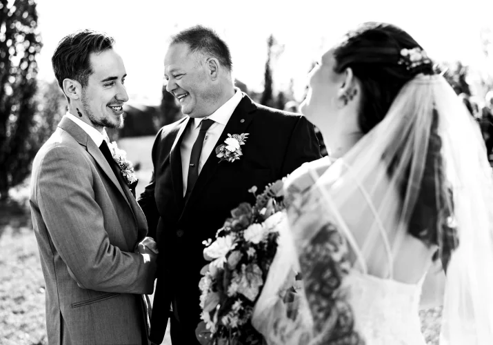 The father of the bride giver her away to the groom. They both laugh while talking.