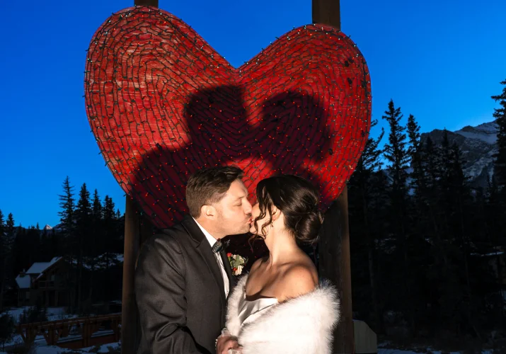Bride and groom share a kiss against big, read wedding heart