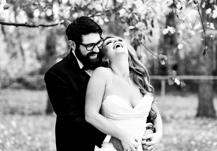 The groom hugs his wife from behind. She laughs in the park in Edmonton.