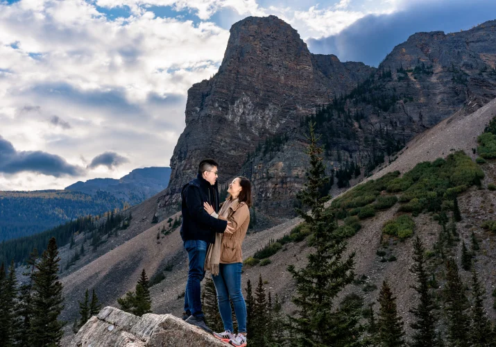 engaged couple in a hug standing at a huge rock in the mountains in Canada