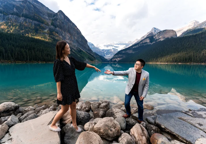 Man helps his fiancee to walk on the rocks at beautiful Lake Louise.