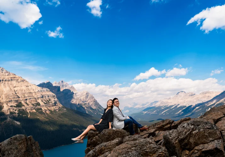 Engaged couple sitting back to back in the mountains at Peyto Lake