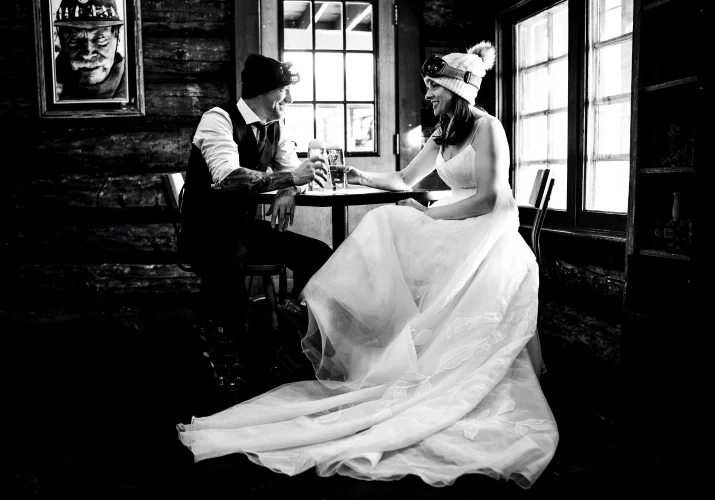 Bride and groom sit by the table and drink a beer.
