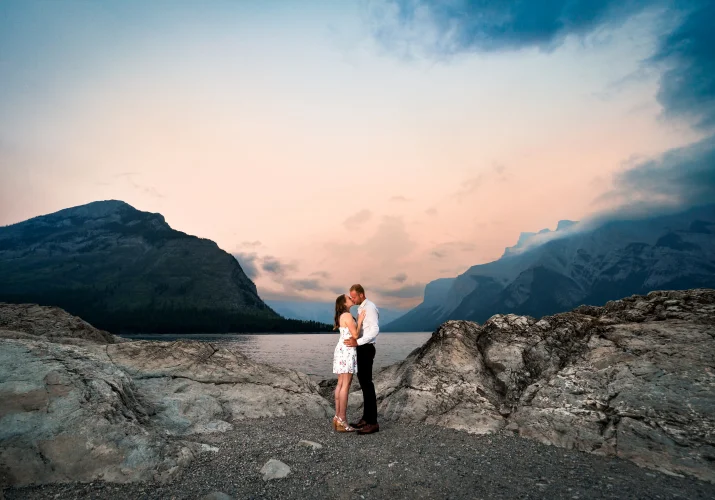young couple share a kiss at the shore of Minnewanka Lake
