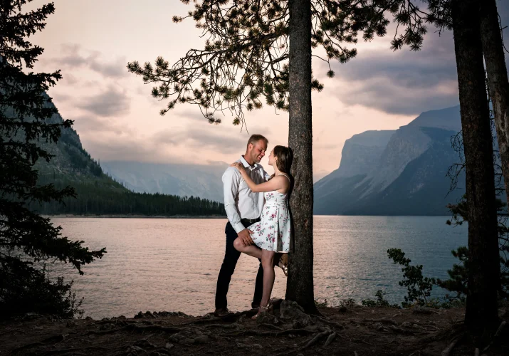 Romantic Banff Engagement photography of the woman leaning over the tree and her fiancee hugging her