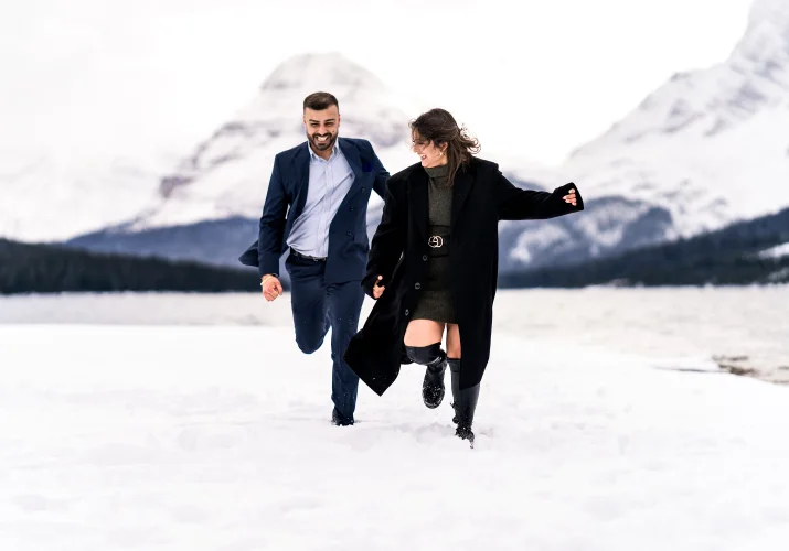 Engaged couple run and have lots of fun in the snow in Banff National Park.