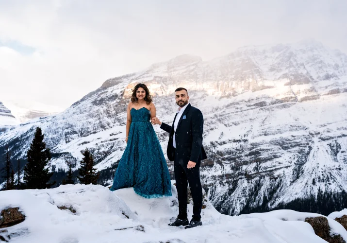 Gentleman helps his fiancee to walk down the small hill covered with snow in Banff National Park