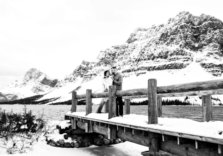 two lovers stand at the wooden bridge at Bow Lake against huge mountain covered with snow.