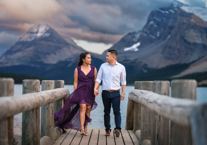 Man and lady in a purple dress walking on the wooden bridge in Banff.