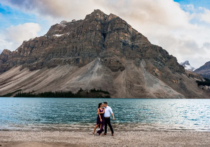 Engaged couple dances at the shore of Bow Lake against huge mountain.