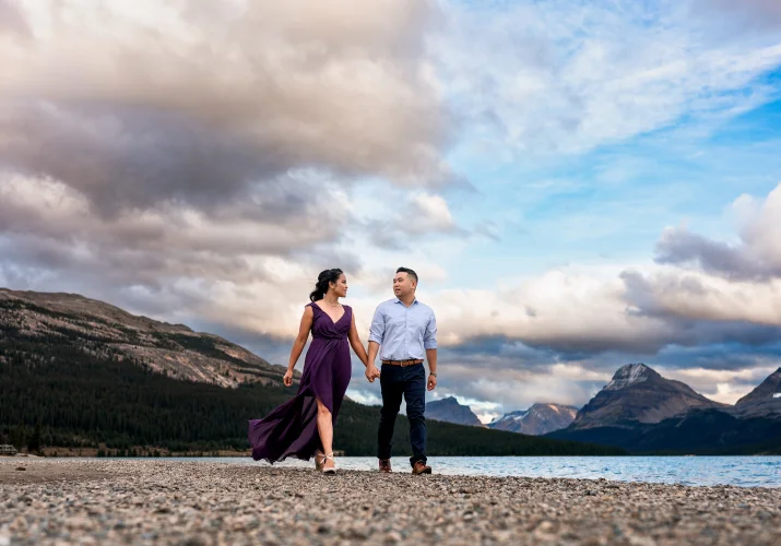Engaged couple walks at the shore of Bow Lake during coloreful sunset.