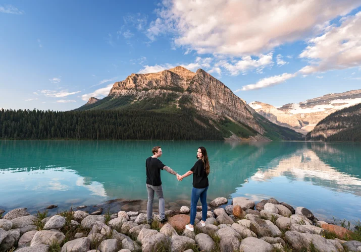 Engaged couple hold hands and adore the stunning view of the Rocky Mountains at Lake Loyuse.