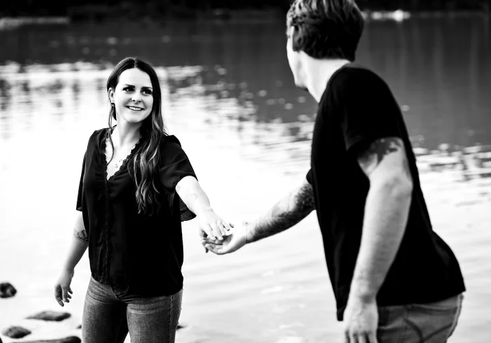 A Man helps his fiancee and gives her hand at the lake.