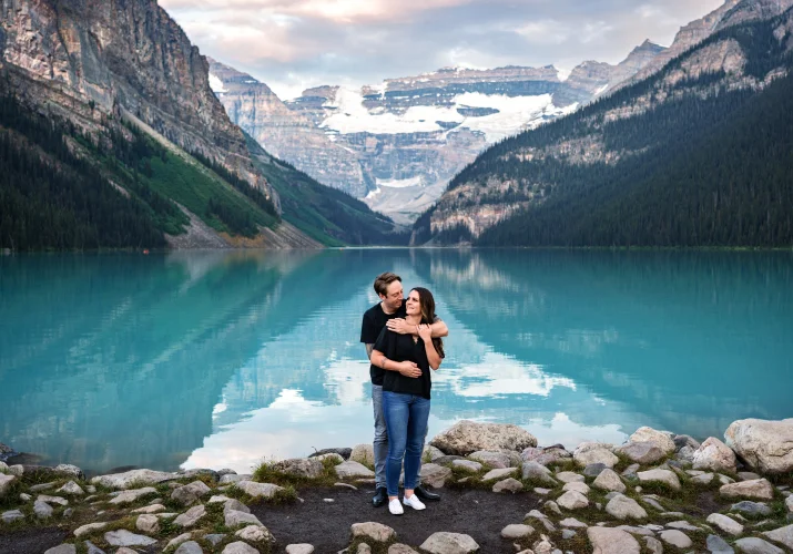 Lake Louise Engagement Photography of the couple in a hug at the shore of turquoise lake.
