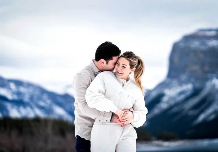 Man hugs his fiance from behind in the mountains