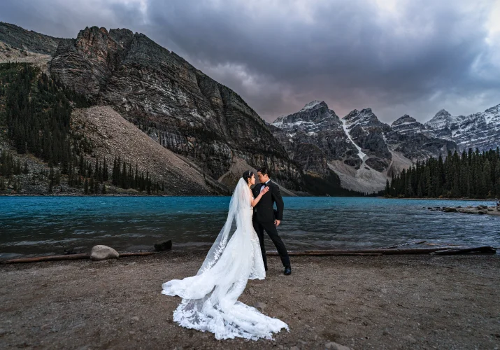 Bride and groom stand at the lakeshore at Moraine Lake