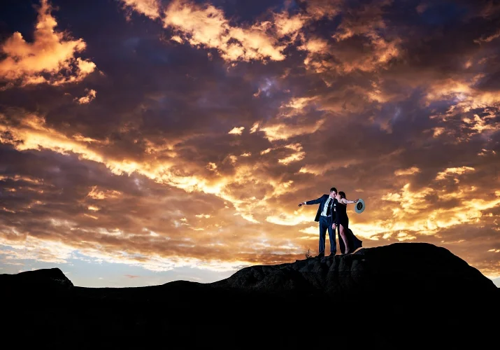 Engaged couple standing up the hill and kissing during colourful sunrise in Calgary. Amazing Engagement and Wedding Photography captured by Lukas SlobodzianL