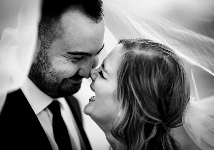 Bride and groom under the veil. They laugh and look deeply info each others eyes.