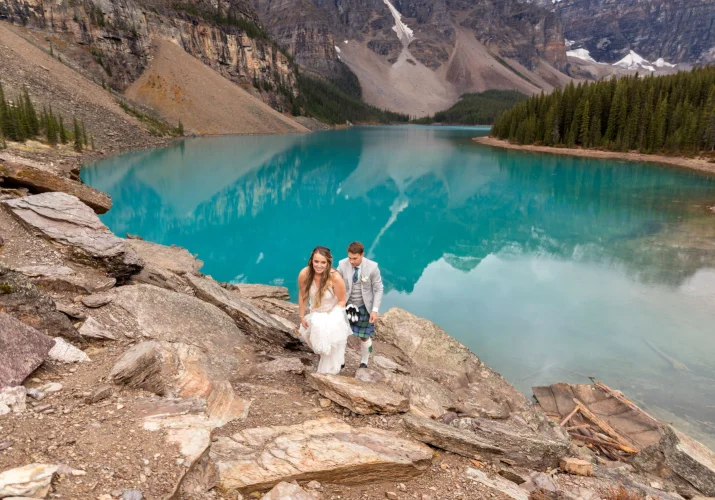 Groom holding the bride's wedding dress while climbing the mountain after wedding ceremony